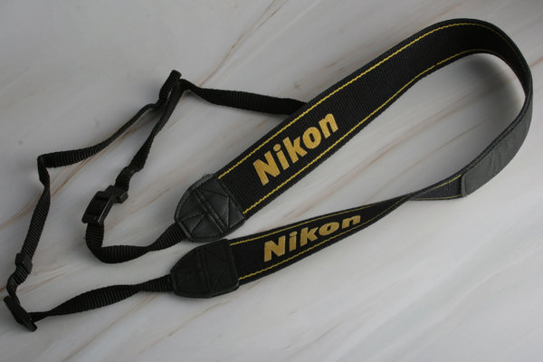 Nikon Kameragurt schwarz mit gelber Schrift und Ziersträngen; gebraucht
